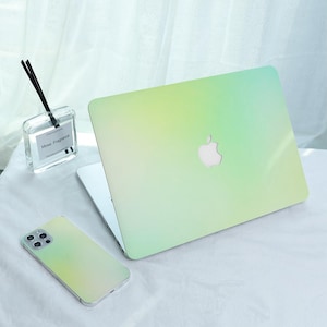 May include: A laptop and smartphone with a gradient green and yellow design. The laptop has a white Apple logo. A clear glass diffuser with black reeds is in the background.