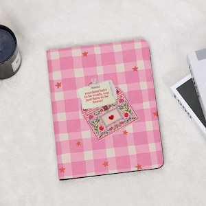 Könnte beinhalten: Ein rosa-weiß kariertes Notizbuch mit einem dekorativen Umschlagdesign. Der Umschlag hat ein Herz- und Blumenmuster mit dem Text "you dont have to be ready, you just have to be brave!" darauf.