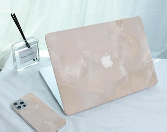 Peut inclure: Un ordinateur portable et un smartphone avec des coques assorties à motif marbre beige. L'ordinateur portable porte le logo Apple blanc. Une bouteille en verre transparent avec des roseaux noirs et le texte "Mose Fragrance" est également visible.
