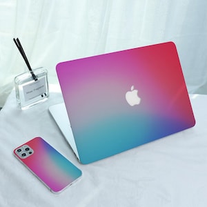 May include: A laptop and a smartphone both featuring a smooth gradient skin that transitions from a vibrant red at the top to a soft purple in the center and a bright cyan blue at the bottom. The laptop displays a centered white Apple logo.