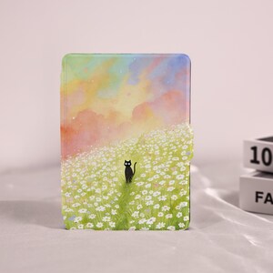 May include: A tablet case with a charming illustration. It depicts a black cat in a field of white daisies, set against a watercolor sky. The case has a magnetic closure and a landscape design.