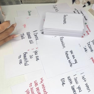 Puede incluir: Una colecci&oacute;n de tarjetas blancas con texto escrito a mano, incluyendo las palabras "Soulmate", "Reunion" y "You are my future wife". Algunas tarjetas tienen tinta roja. Las tarjetas est&aacute;n esparcidas sobre una superficie blanca.