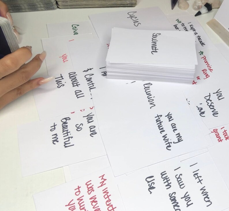 Puede incluir: Una colecci&oacute;n de tarjetas blancas con texto escrito a mano, incluyendo las palabras "Soulmate", "Reunion" y "You are my future wife". Algunas tarjetas tienen tinta roja. Las tarjetas est&aacute;n esparcidas sobre una superficie blanca.