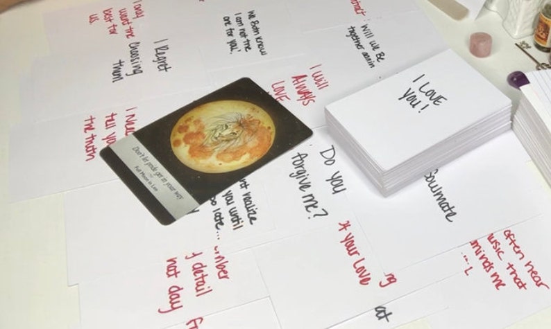 Puede incluir: Una colecci&oacute;n de tarjetas blancas con frases escritas a mano y una pila de tarjetas con "I LOVE YOU!" escrito en ellas. Tambi&eacute;n hay una sola tarjeta con una ilustraci&oacute;n de luna llena. Las tarjetas est&aacute;n esparcidas sobre una superficie blanca.