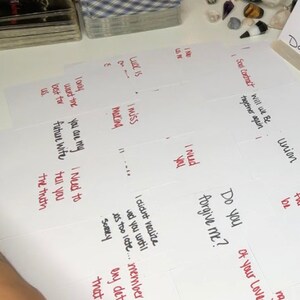 Puede incluir: Una colecci&oacute;n de cartas del tarot y notas manuscritas en tarjetas blancas. Las notas incluyen frases como "Te echo de menos", "&iquest;Me perdonas?" y "Contrato del alma". Se ve una baraja de cartas con un patr&oacute;n azul y blanco.