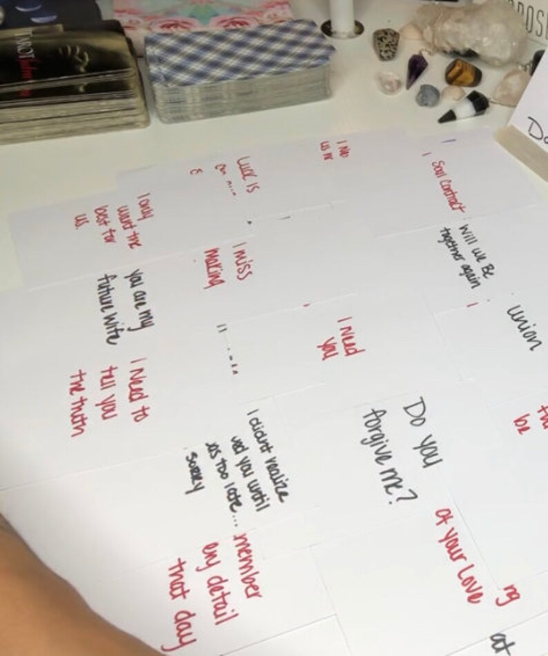 Puede incluir: Una colecci&oacute;n de cartas del tarot y notas manuscritas en tarjetas blancas. Las notas incluyen frases como "Te echo de menos", "&iquest;Me perdonas?" y "Contrato del alma". Se ve una baraja de cartas con un patr&oacute;n azul y blanco.