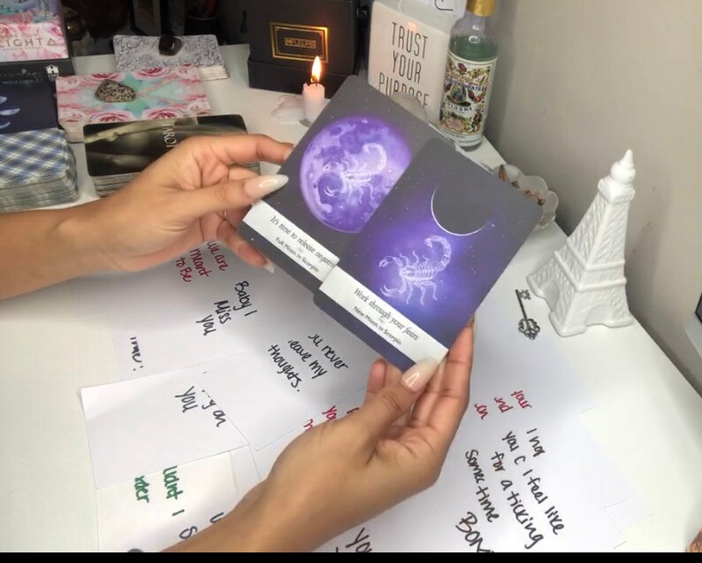 Puede incluir: Se muestran dos cartas de tarot con dise&ntilde;os celestiales. Una carta presenta una luna llena p&uacute;rpura y el texto "It's time to release anyone". La otra carta muestra una luna creciente y un escorpi&oacute;n con el texto "Work through your fears".