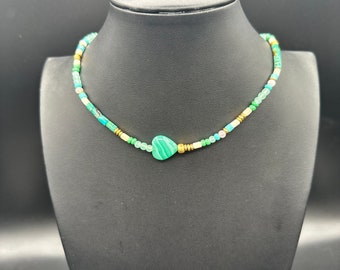 May include: A green and gold beaded necklace with a heart-shaped green stone pendant.