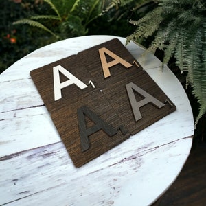 May include: Four wooden letter tiles, each with the letter "A" and the number "1" printed on them. The tiles are in different colors: white, light brown, dark brown, and gray.