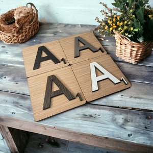 May include: Four wooden coasters with the letter "A" in black, gray, brown, and white. Each coaster has a score of "1" on the bottom right corner. The coasters have a light brown wood grain pattern.