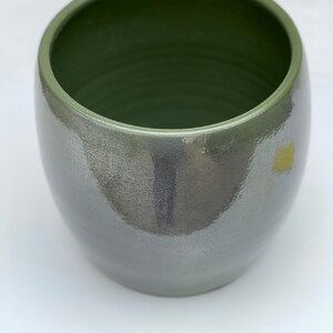 May include: A green ceramic planter with a glossy finish. The planter has a rounded shape and a wide opening.
