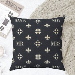 May include: Black and white throw pillow with a repeating pattern of fleur-de-lis and a diamond shape. The words "MR" and "MRS" are repeated in a white font on the pillow.