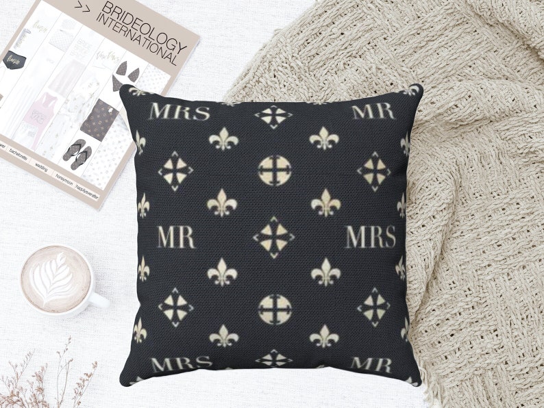 May include: Black and white throw pillow with a repeating pattern of fleur-de-lis and a diamond shape. The words "MR" and "MRS" are repeated in a white font on the pillow.
