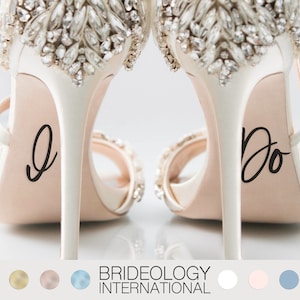 May include: A pair of white high-heeled shoes with rhinestones on the top. The soles of the shoes have the words "I do" and "Do" written on them.