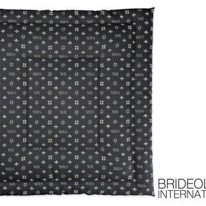 May include: A black quilted throw blanket with a repeating pattern of "MR" and "MRS" in a light beige color. The pattern also includes a small fleur-de-lis design. The blanket has a stitched border.