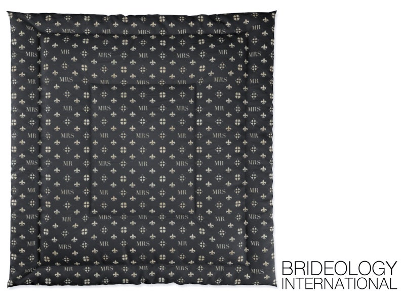 May include: A black quilted throw blanket with a repeating pattern of "MR" and "MRS" in a light beige color. The pattern also includes a small fleur-de-lis design. The blanket has a stitched border.