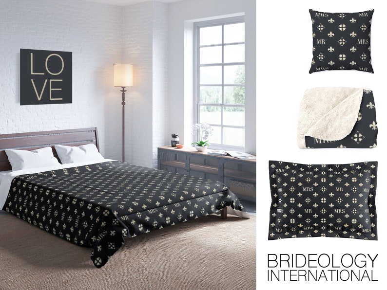 May include: A black and white patterned throw blanket with a white sherpa lining. The blanket features a repeating pattern of fleur-de-lis and the words "Mr." and "Mrs." in a script font. The blanket is displayed on a bed with a black and white patterned duvet cover. The word "LOVE" is displayed on a black square canvas on the wall behind the bed.
