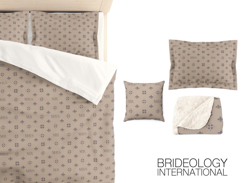 Puede incluir: Un juego de cama beige y marr&oacute;n con un patr&oacute;n repetido de "MR" y "MRS" con un dise&ntilde;o de flor de lis. El juego incluye una funda n&oacute;rdica, dos fundas de almohada, un coj&iacute;n y una manta.
