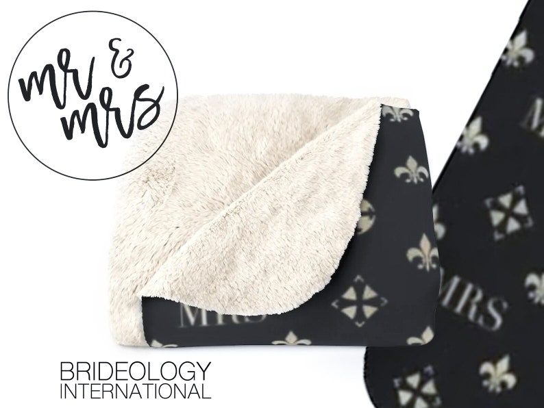 May include: A black and white throw blanket with a repeating pattern of fleur-de-lis and a stylized cross. The blanket has a white sherpa lining and the words "Mr. & Mrs." are printed on the front.