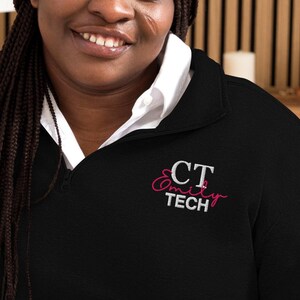 Könnte beinhalten: Schwarzer Pullover mit einem weißen gestickten Logo, das "CT Amity Tech" in rosa Schrift zeigt.