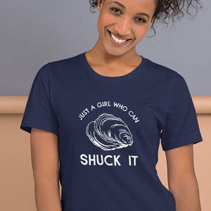 May include: A navy blue t-shirt with a white graphic of an oyster and the text "Just a girl who can shuck it".