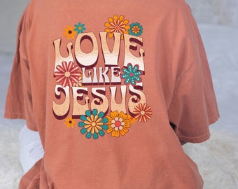 May include: A rust-colored t-shirt with a retro-style graphic that says "Love Like Jesus" surrounded by colorful flowers.