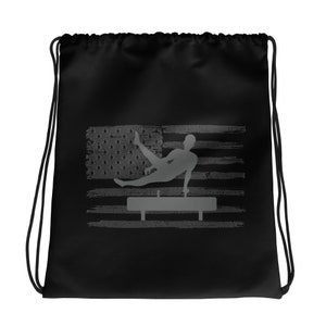 May include: Black drawstring bag featuring a gray silhouette of a gymnast performing on a pommel horse, set against a distressed American flag design. The bag has black drawstrings.