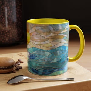 May include: A yellow ceramic mug with a stained glass design of a sun setting over a blue ocean. The mug has a handle and is perfect for enjoying a hot beverage.