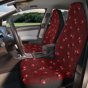 May include: Red car seat covers with a cherry print. The covers are made of a soft, comfortable fabric and feature a unique design.