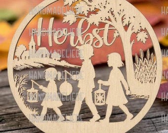 May include: A circular light-colored wooden cutout featuring a laser-cut scene of three children carrying lanterns under a tree and near a church. The word "Herbst" is inscribed in cursive script at the top center of the circular wooden ornament.