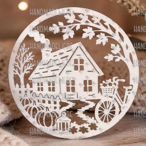 May include: A circular white wooden ornament featuring a laser-cut design of a house with a chimney, a bicycle with a basket, pumpkins, and a fence, all framed by tree branches and leaves, creating a detailed silhouette of a rural scene.