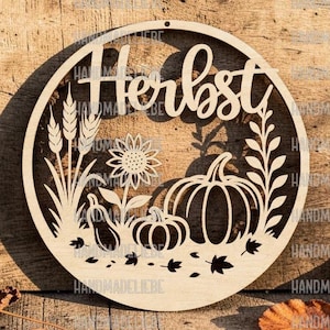 Puede incluir: Un adorno de pared circular de madera clara con un diseño cortado a láser que muestra espigas de trigo, un girasol, dos calabazas y hojas dispersas. La palabra Herbst está recortada en letra cursiva en la parte superior del marco.