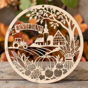 May include: A circular light-coloured wooden cutout featuring a laser-cut design of a tractor, a church, a half-timbered house, a tree, wheat, a pumpkin, apples, and grapes. The text "ERNTEDANK" is displayed on a banner across the top.