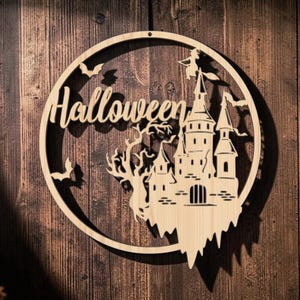 Könnte beinhalten: Ein kreisförmiger Wandbehang aus hellem Holz mit einem lasergeschnittenen Motiv aus einer Burg, einem kahlen Baum, fliegenden Fledermäusen und einer Hexe auf einem Besen. Das Wort Halloween ist in Schreibschrift im oberen Teil ausgeschnitten.