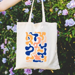 a person holding a tote bag in front of purple flowers