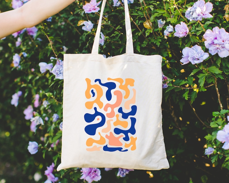 a person holding a tote bag in front of purple flowers