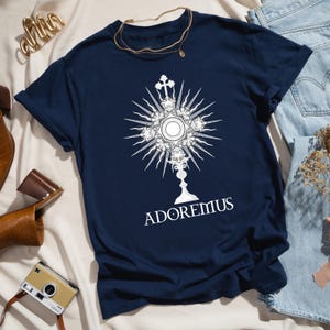 Catholic t-shirt featuring a white Eucharistic monstrance graphic with rays and the word 'Adoremus' below—perfect for Adoration, church events, or spiritual wear.