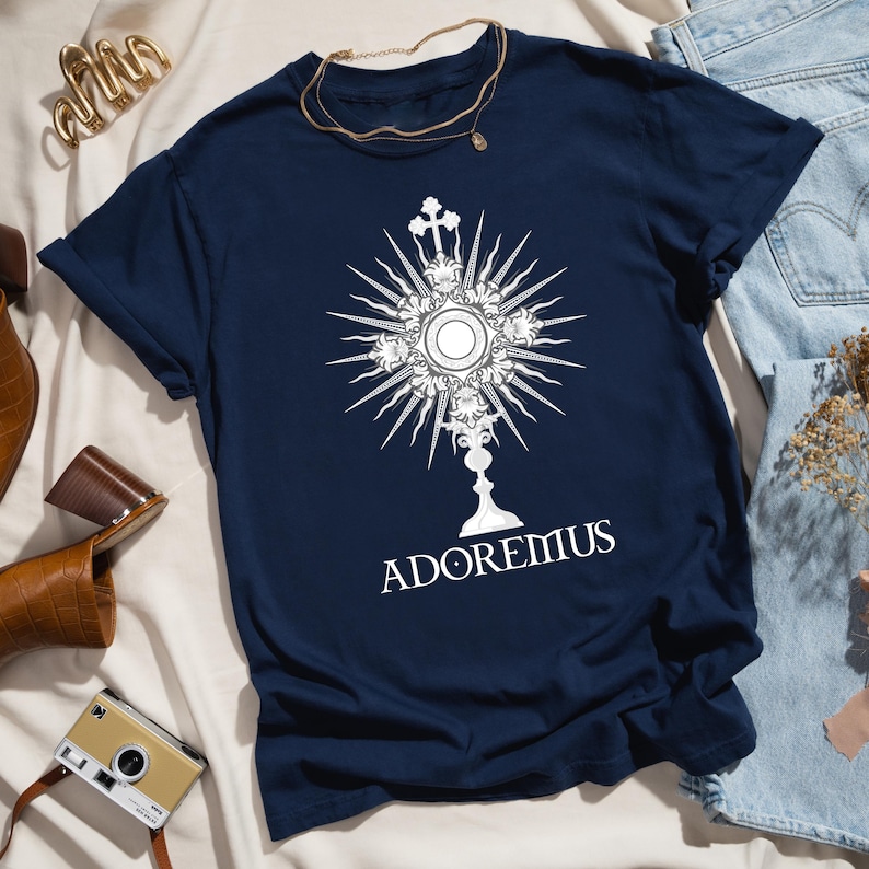 Catholic t-shirt featuring a white Eucharistic monstrance graphic with rays and the word 'Adoremus' below—perfect for Adoration, church events, or spiritual wear.