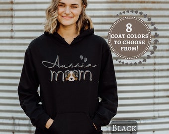 Puede incluir: Sudadera con capucha negra con un gráfico blanco que dice "Aussie Mom" y un perro pastor australiano de dibujos animados. La sudadera tiene una capucha con cordón y un bolsillo canguro.