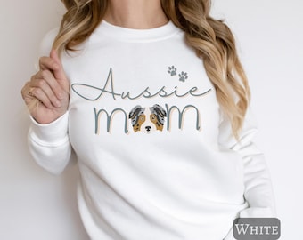 Puede incluir: Sudadera blanca con el texto "Aussie Mom" en una fuente cursiva con una ilustración de perro pastor australiano azul y marrón y huellas de patas.