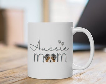 May include: White ceramic mug with a grey and black graphic of an Australian Shepherd dog and the text "Aussie Mom" with paw prints.