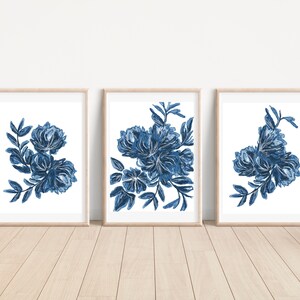 以下が含まれることがあります： 青い水彩画の花のイラストが描かれた額装されたプリント3枚。それぞれのプリントは、青い花と葉の異なる配置が特徴です。