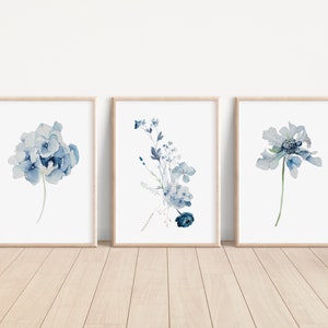 Puede incluir: Conjunto de tres impresiones de acuarela con flores azules. Las impresiones están enmarcadas en marcos de madera natural y son perfectas para agregar un toque de naturaleza a cualquier habitación.