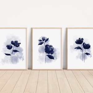 May include: Set of three watercolor prints featuring abstract blue floral illustrations on a white background. The prints are framed in natural wood frames.