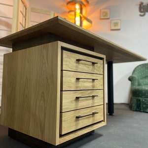 Peut inclure: Un bureau en bois avec un bloc de tiroirs comprenant quatre tiroirs avec des poignées en métal noir. Le bureau est en bois clair avec un grain naturel.
