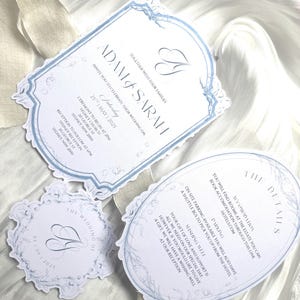 以下が含まれることがあります： 3枚のカードからなる結婚式の招待状セット。メインの招待状は、白地に水色の縁取りで、「ADAM & SARAH」と結婚式の詳細が書かれています。他のカードには詳細と結婚式のロゴが含まれています。