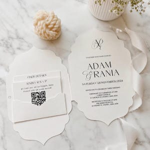 May include: A die-cut wedding invitation suite with scalloped edges featuring the names Adam and Rania, a date of November 25, 2024, and event details. The set includes a pocket containing a card with Finer Details and a QR code for RSVP.