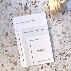 May include: A stack of white wedding invitation cards with black text. The cards read "We can't wait to celebrate with you," "05.05.25," "The finer details," "The wedding of," and the names "ANTHONY AND NADIA."