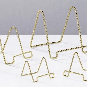 May include: Set of six gold metal display stands in various sizes. The stands are made of twisted wire and have a triangular shape.