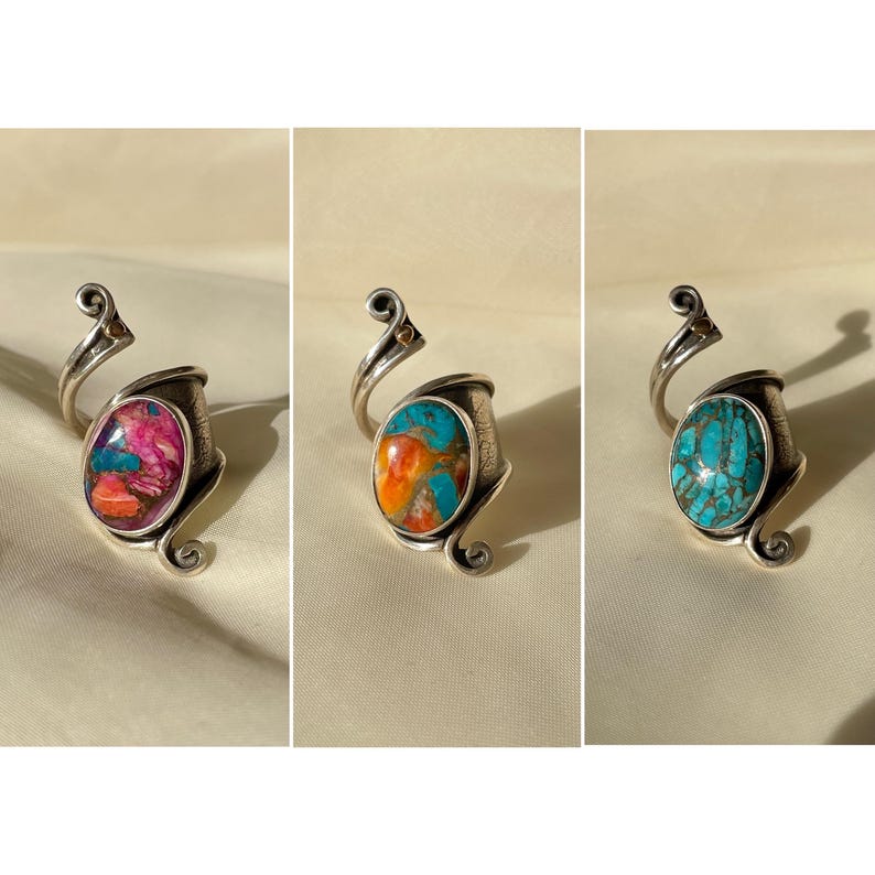 May include: Three silver rings with unique oval-shaped gemstones. The rings have a swirling design and are set on a white fabric background.